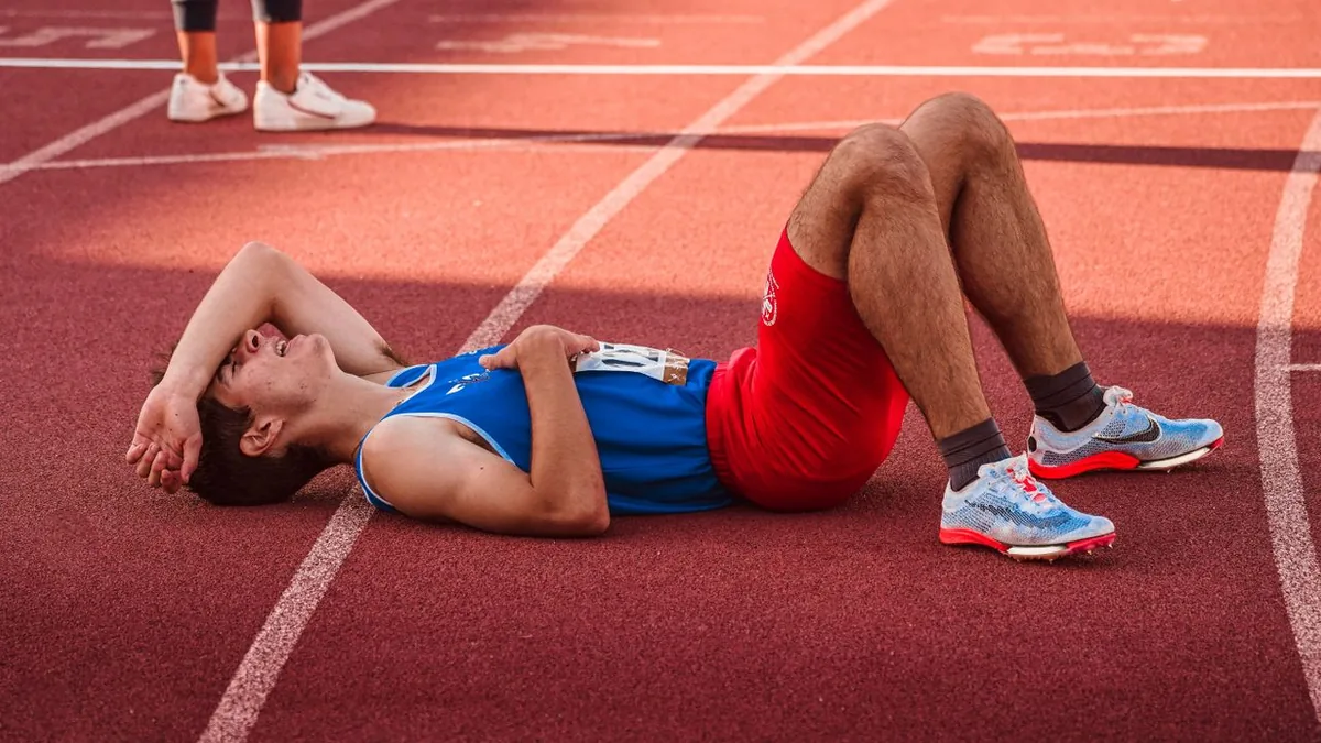 Coureur allongé sur la piste, le bras sur le front, après une course