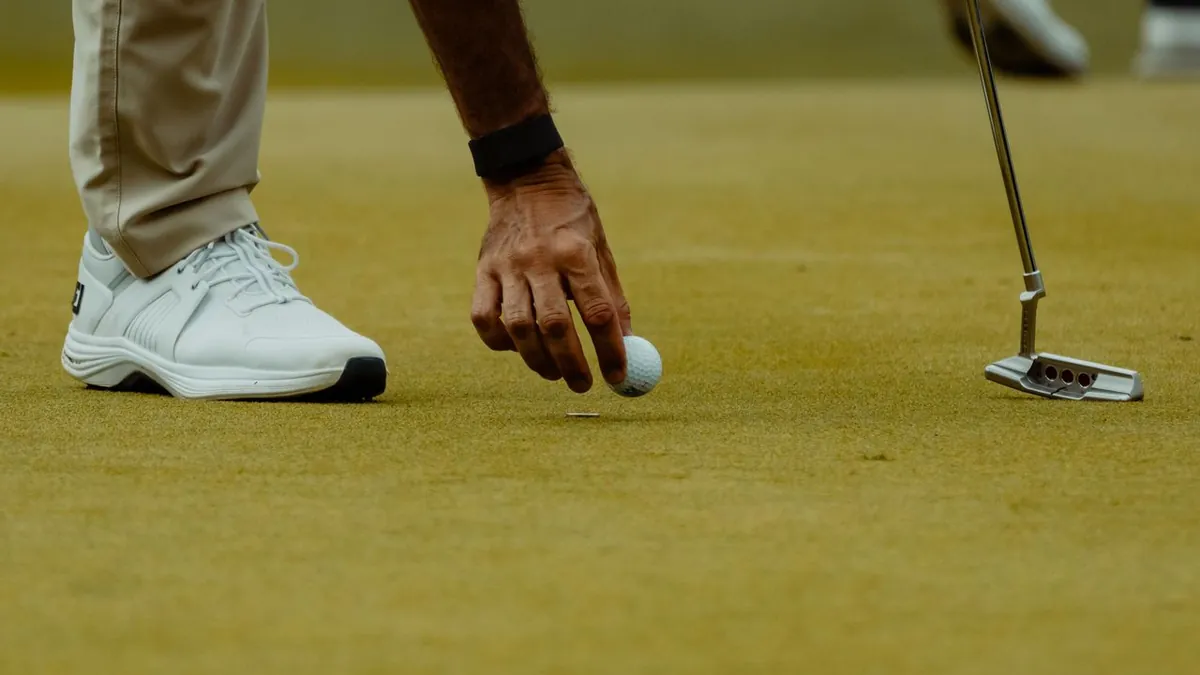 Golfeur qui ramasse sa balle sur le green, putter planté à côté de lui